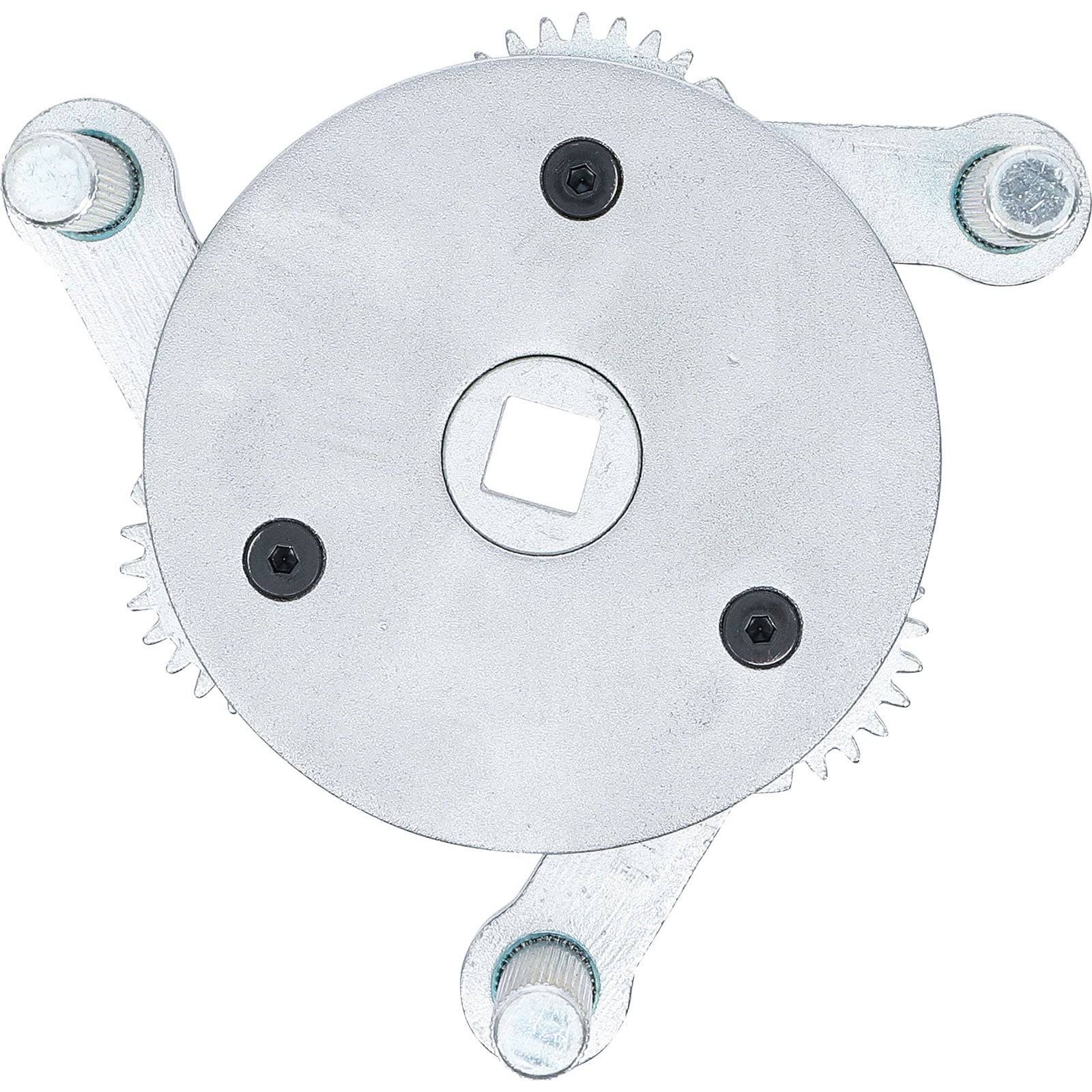 Ein kreisförmiges Metallinstrument mit drei verstellbaren Armen und Zahnrädern, das zum Greifen oder Festziehen verwendet wird, vor einem einfarbigen Hintergrund.