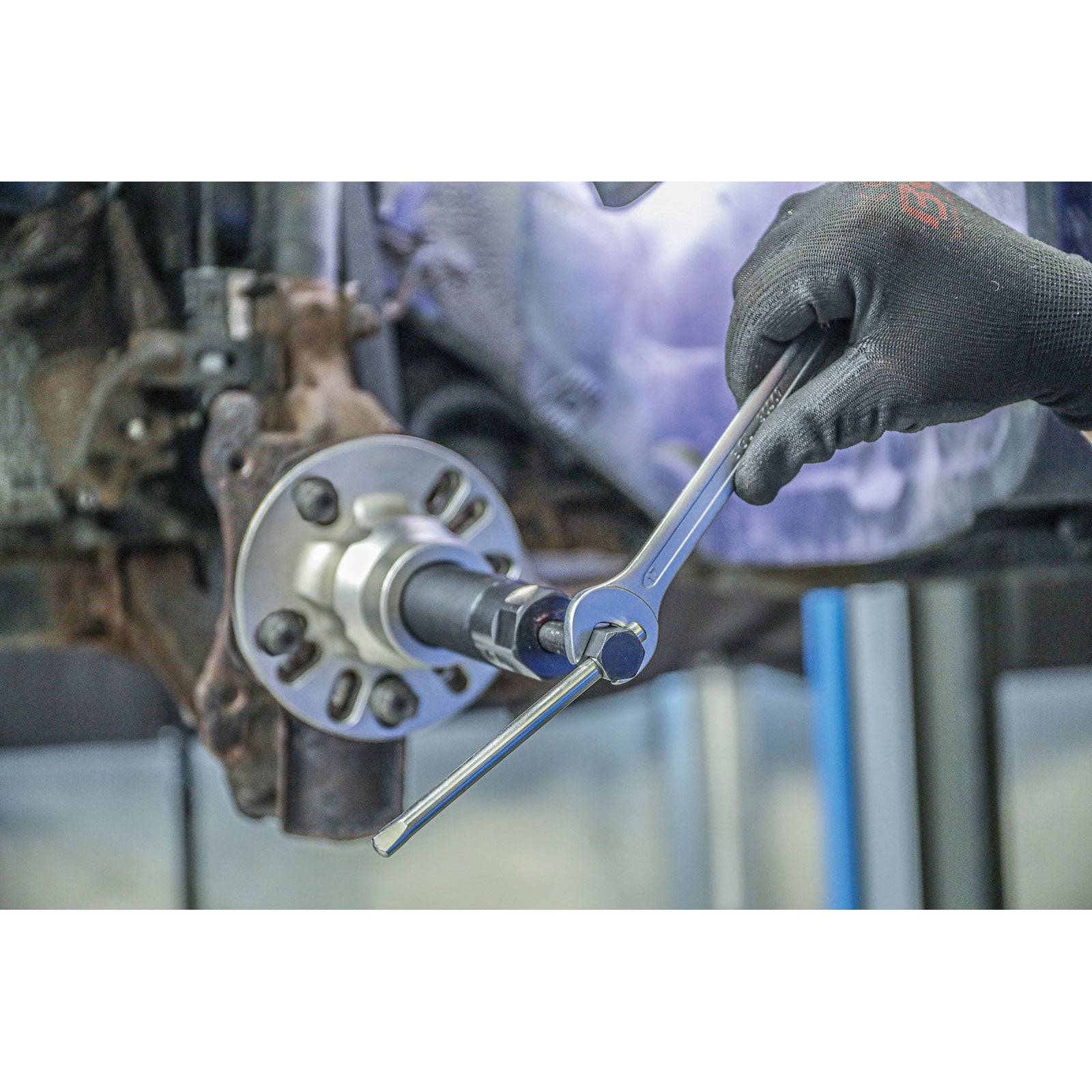 Eine Person trägt Handschuhe und verwendet einen Schraubenschlüssel, um an einem Fahrzeugteil zu arbeiten. Sie scheint eine Komponente in der Nähe einer Radnabe anzupassen oder einzubauen.