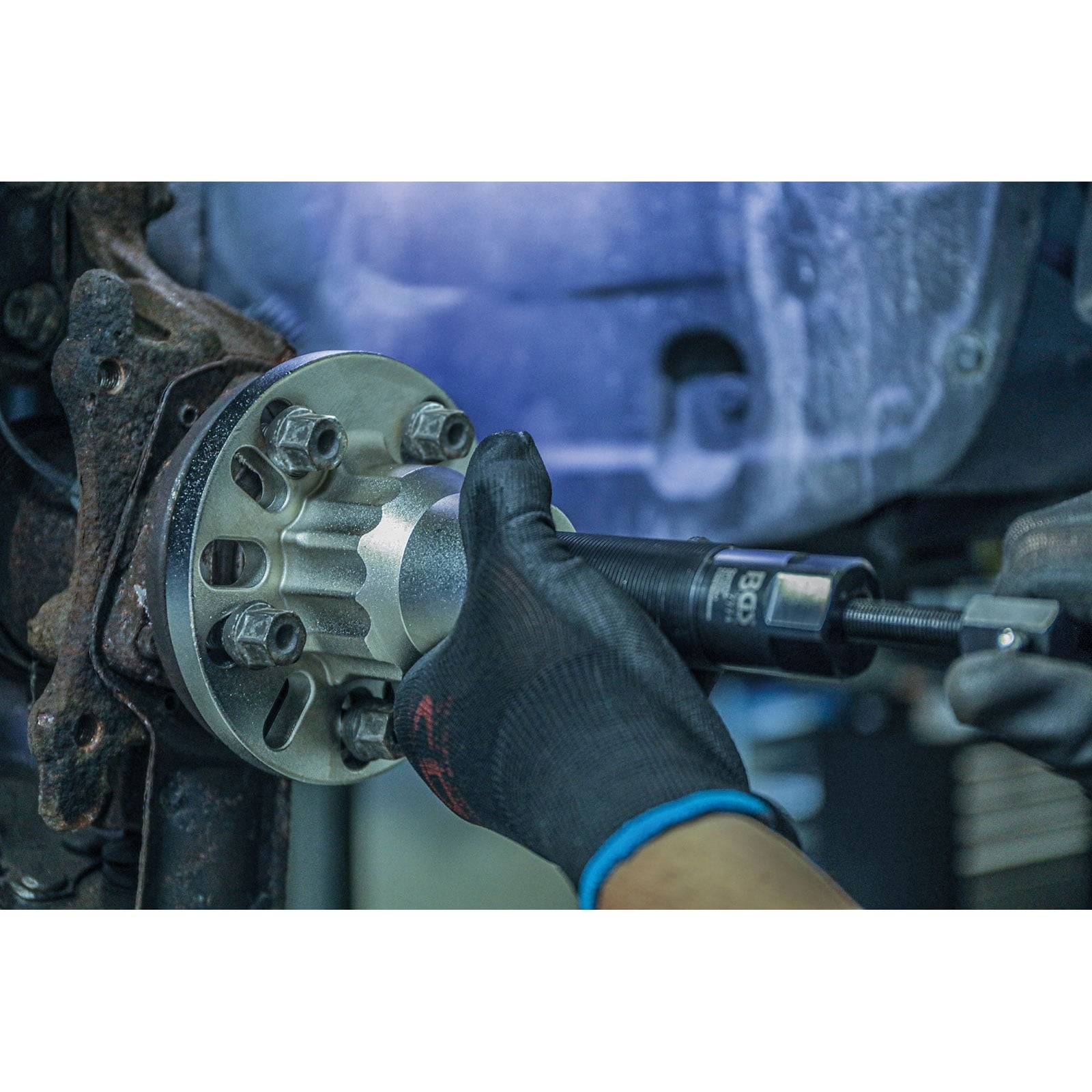 Eine behandschuhte Hand benutzt ein Werkzeug, um Bolzen an einer Fahrzeugrradnabe festzuziehen, was laufende Wartungsarbeiten im Automobilbereich demonstriert.