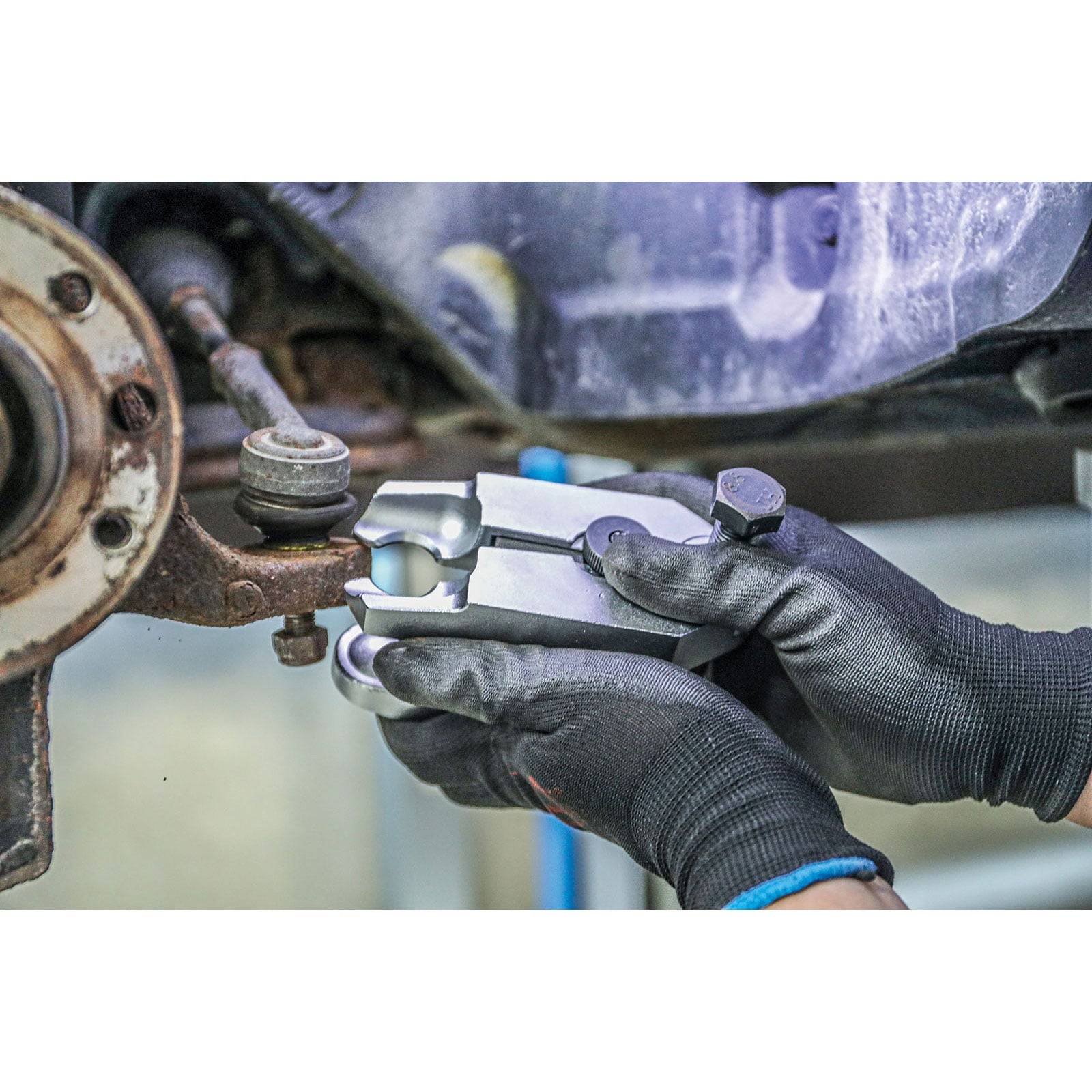 Ein Mechaniker, der schwarze Handschuhe trägt, verwendet eine Bremssattelschieblehre, um die Dicke und Abnutzung der Bremsscheibe eines Autos in einer Werkstattumgebung zu messen.