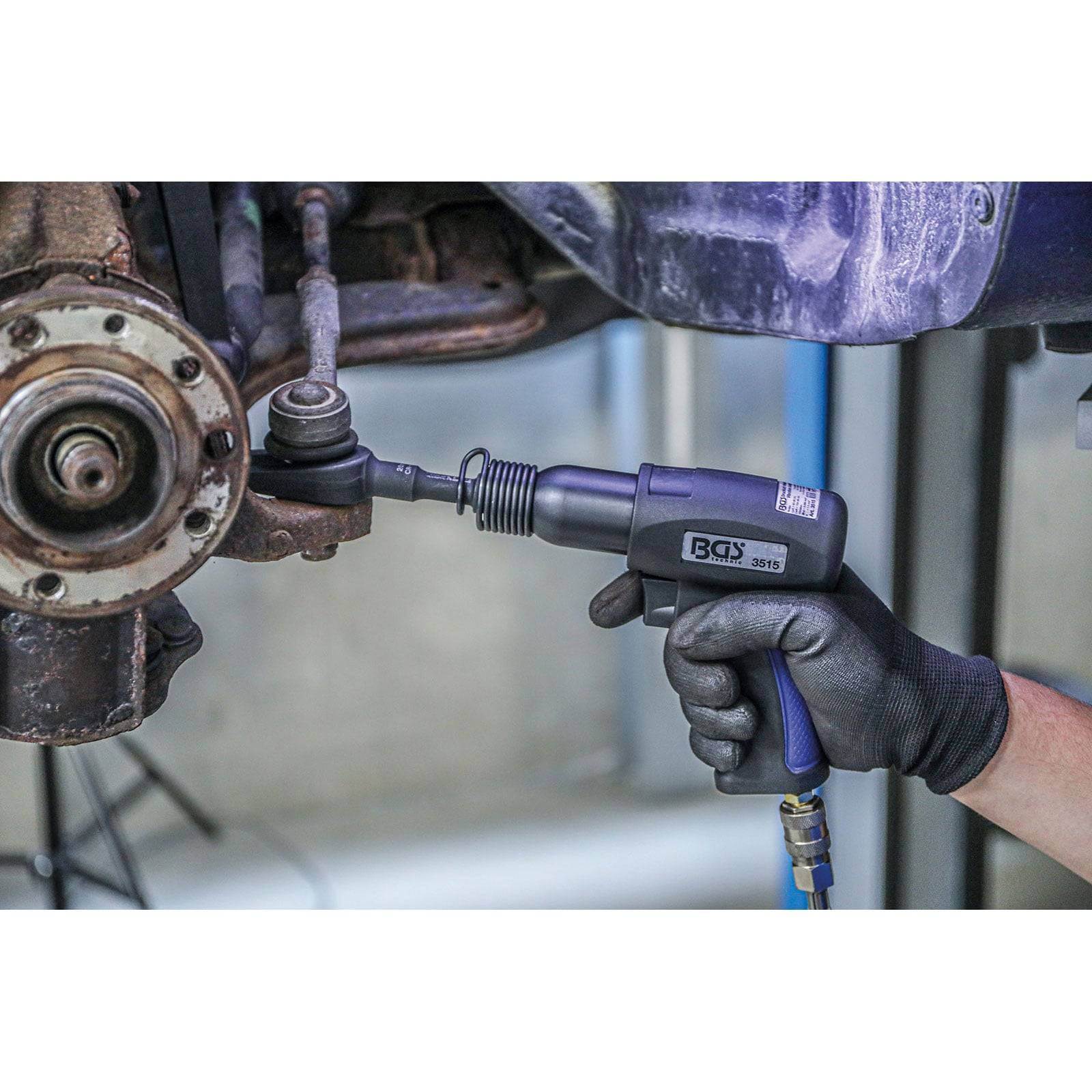 Ein Mechaniker verwendet eine Druckluft-Schlagschrauber, um eine Schraube am Fahrwerksystem eines Fahrzeugs festzuziehen und veranschaulicht damit Arbeiten zur Fahrzeugwartung.