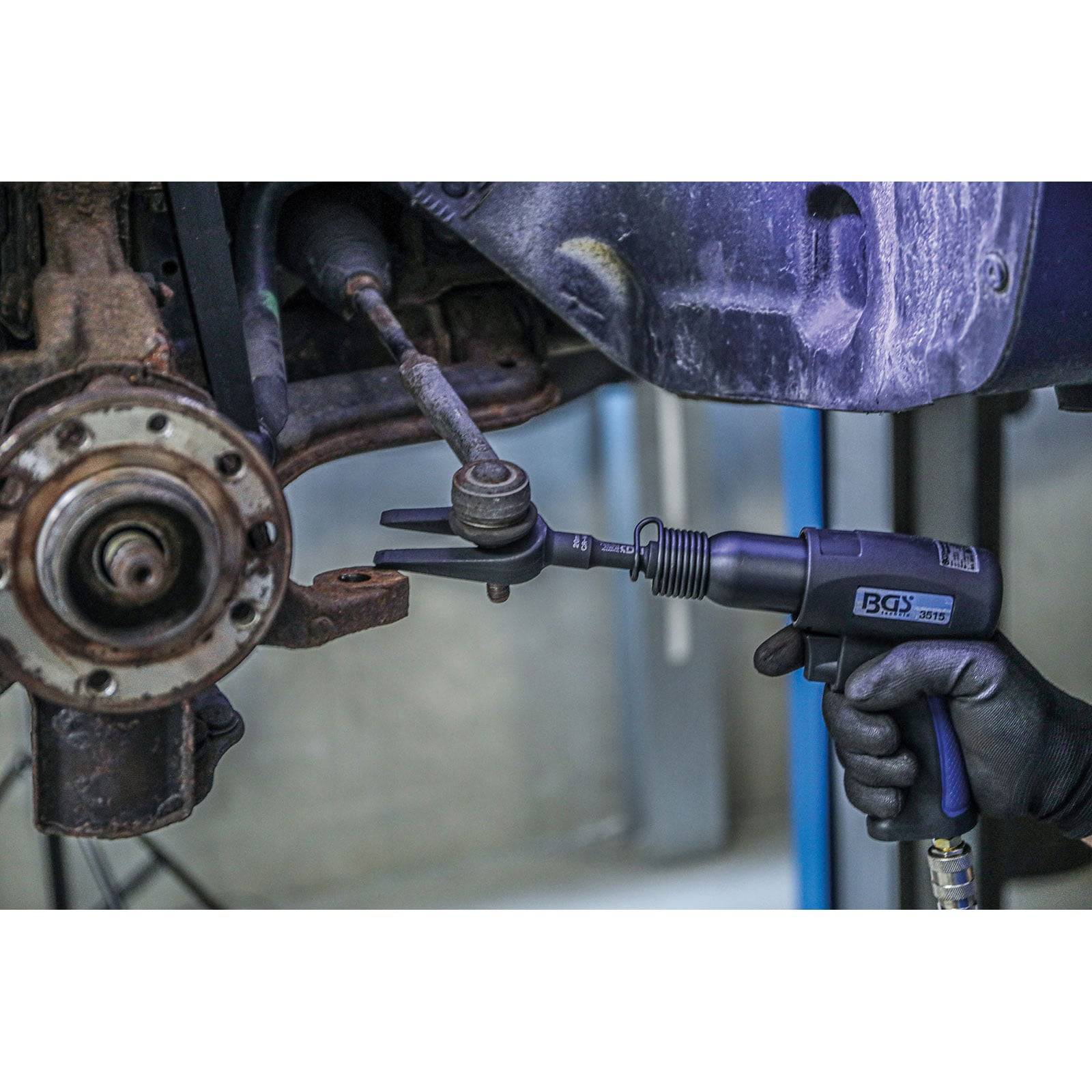 Ein Mechaniker verwendet ein Schlagwerkzeug, um ein Kugelgelenk im Fahrwerksystem eines Autos in einer Werkstatt zu lösen.