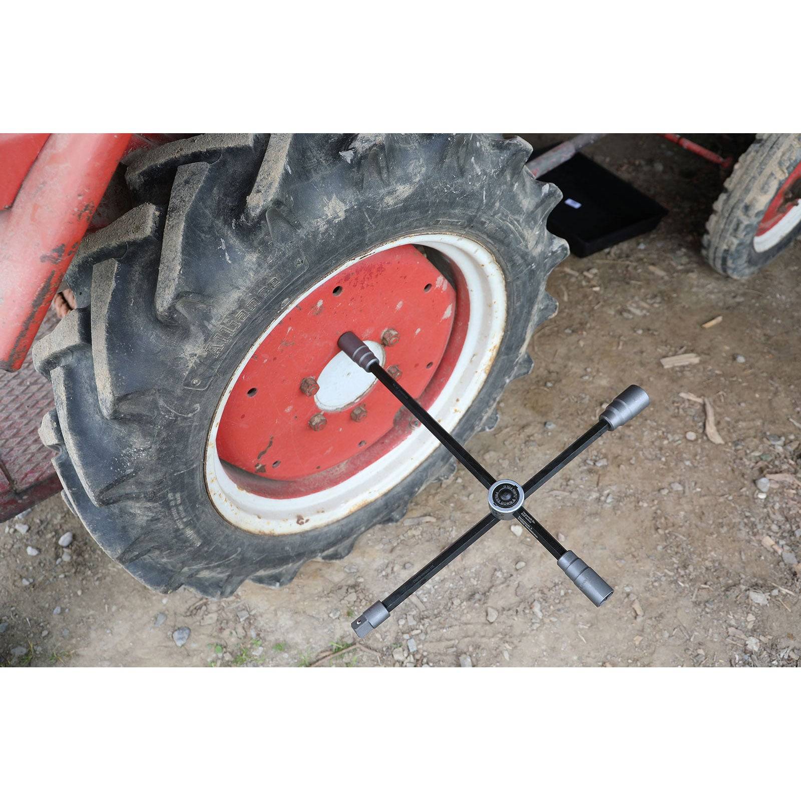 Ein rotes Traktorrad auf einem Erdgrund mit einem Kreuzschlüssel, der auf dem Rad positioniert ist und auf Radwartung oder Reifenwechsel hinweist.