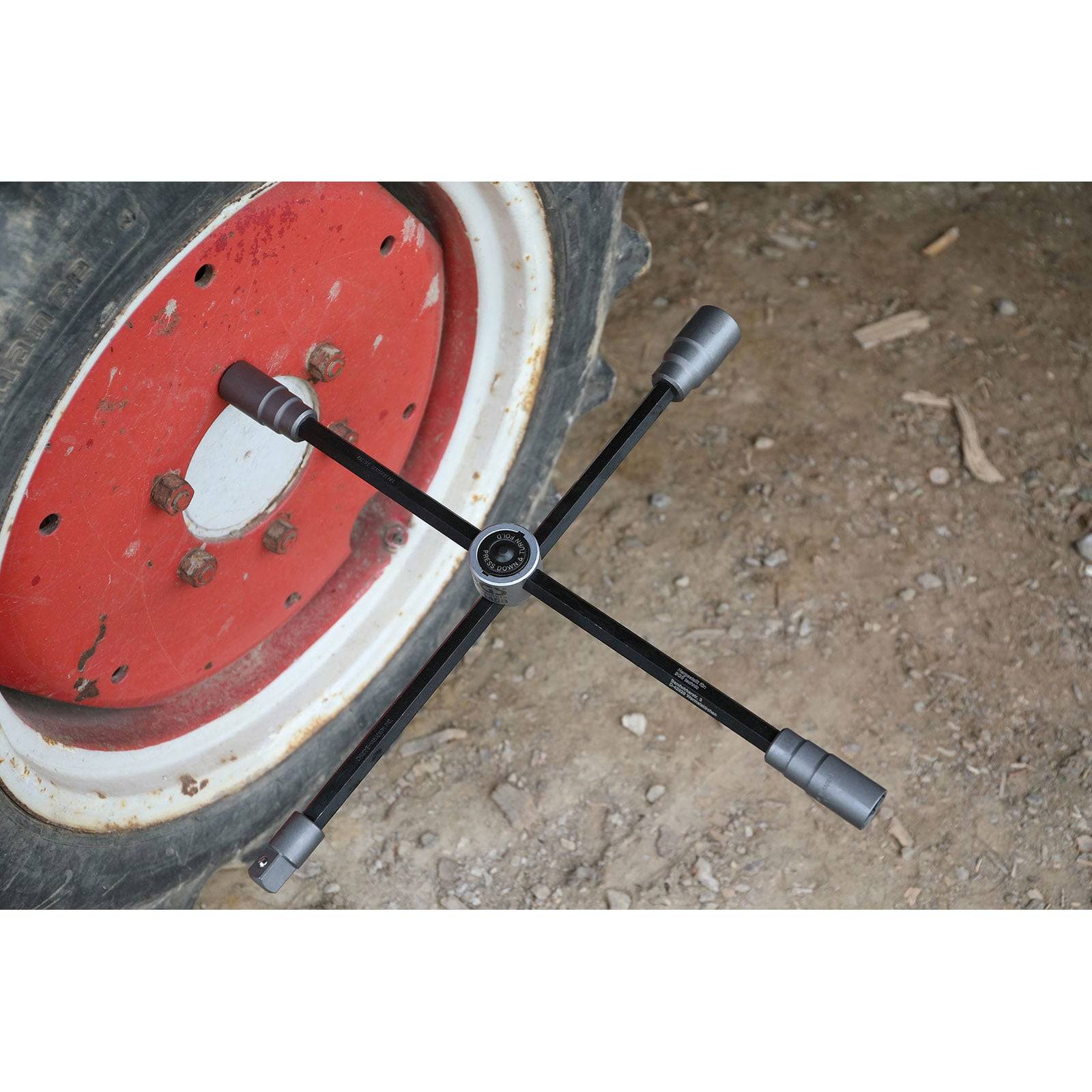 Ein Radkreuz wird auf der Nabe eines roten und weißen Rades abgelegt, das auf einem Erdgrund ruht und damit auf einen Reifenwechsel oder eine Wartung hinweist.