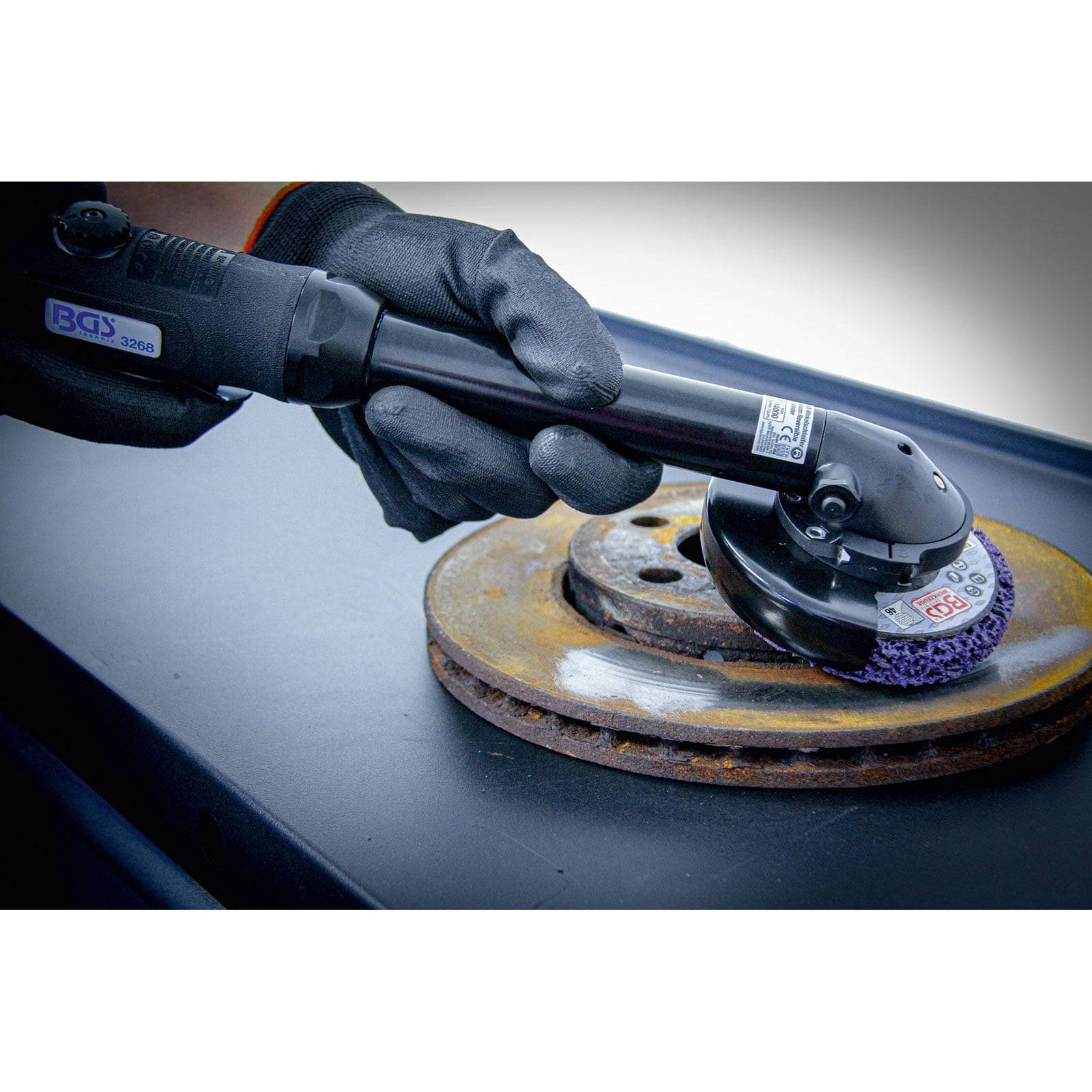 Eine Person mit Handschuhen verwendet einen Winkelschleifer mit einer lila Schleifscheibe, um Rost von einer Metalloberfläche zu schleifen.