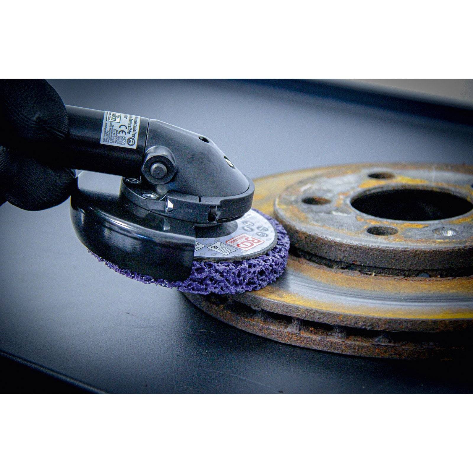 Eine Nahaufnahme eines Elektrowerkzeugs mit einem Schleifpad, das eine rostige Metalscheibe poliert und dabei den Oberflächenreinigungs- und Restaurierungsprozess demonstriert.