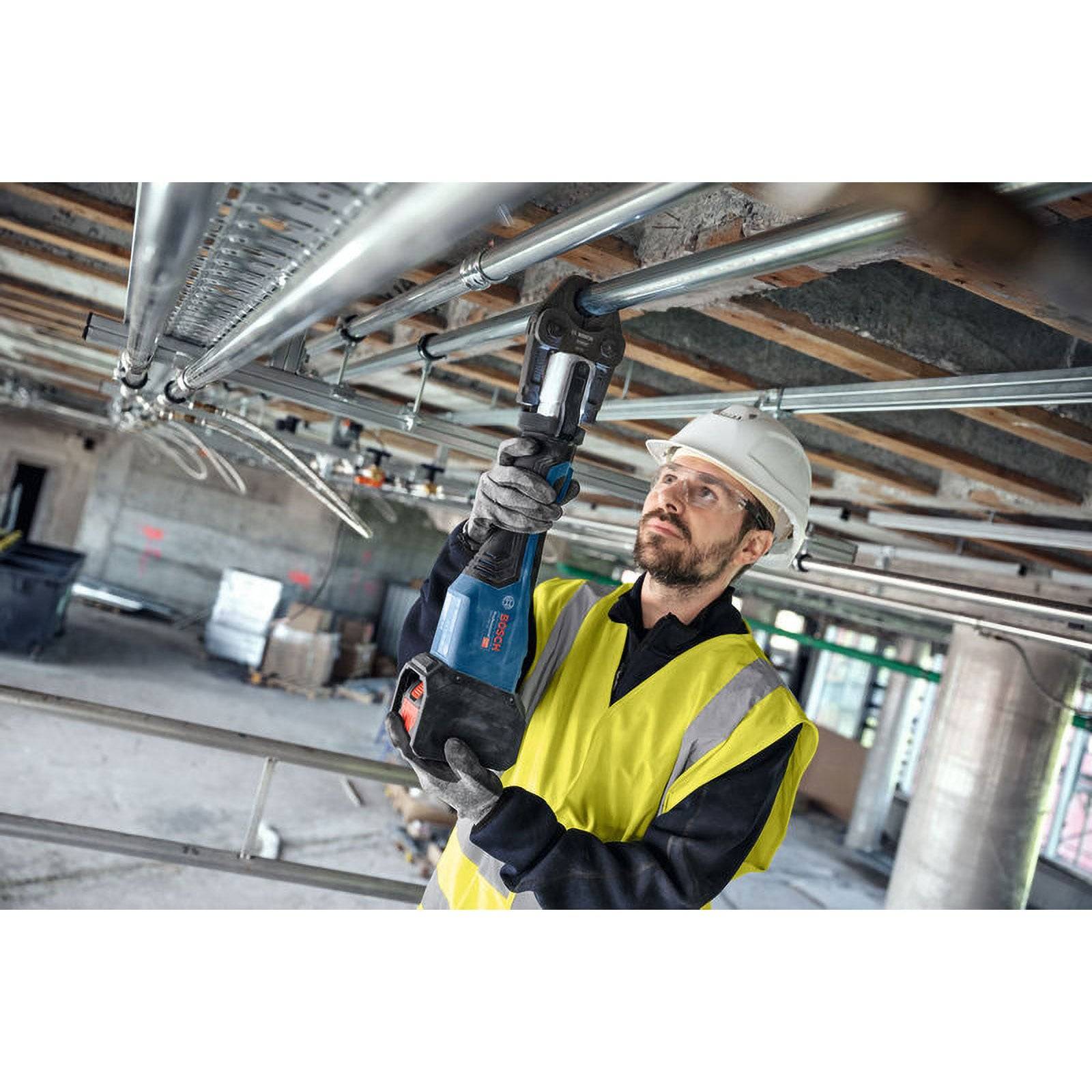 Ein Bauarbeiter in einem Schutzhelm und einer Warnweste verwendet ein Elektrowerkzeug, um Metallrohre auf einer Baustelle einzustellen.