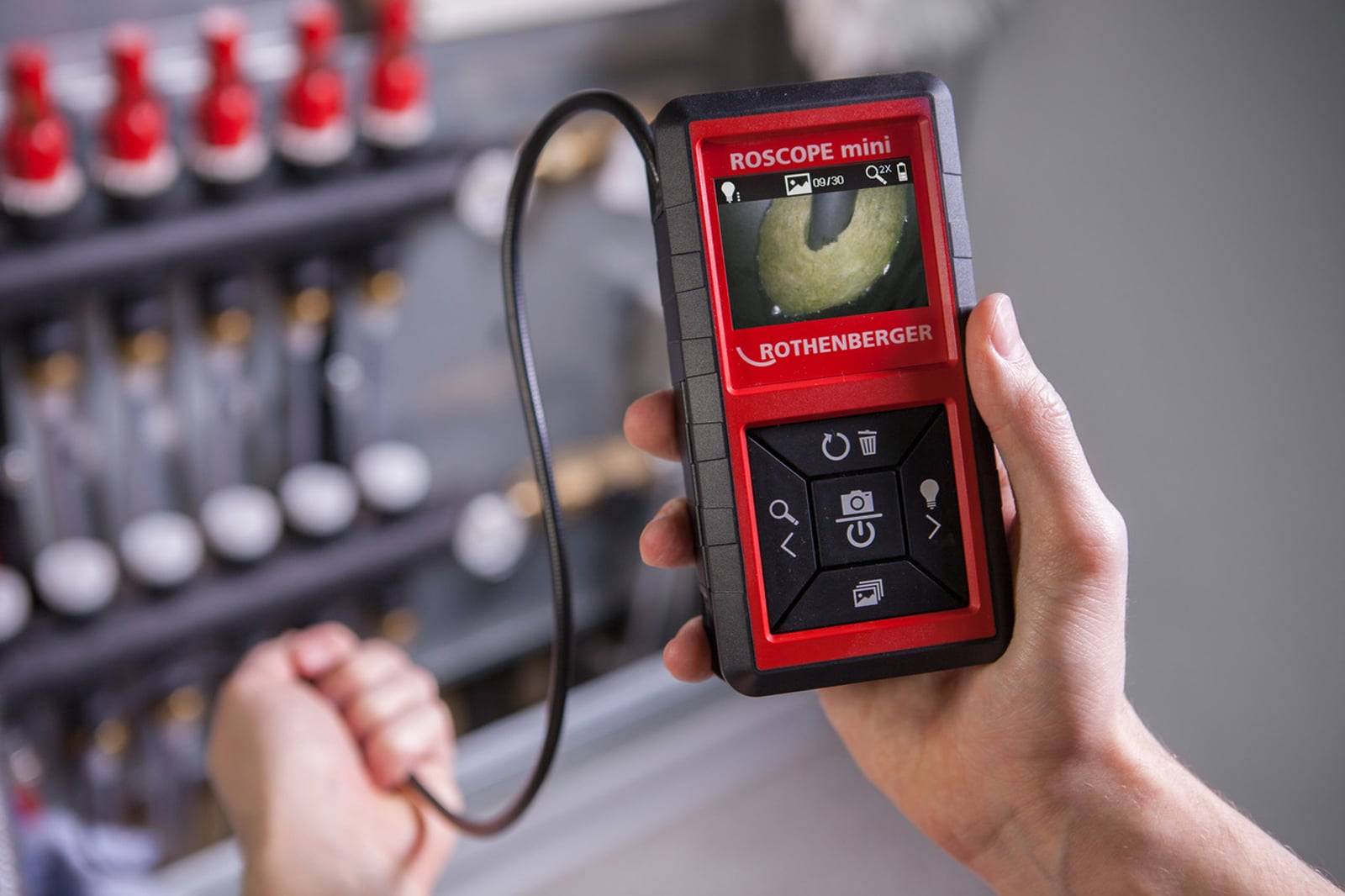 Eine Person verwendet ein tragbares Inspektionskamera-Gerät, das das Rohrinnere auf dem Bildschirm anzeigt, in einem industriellen Umfeld.