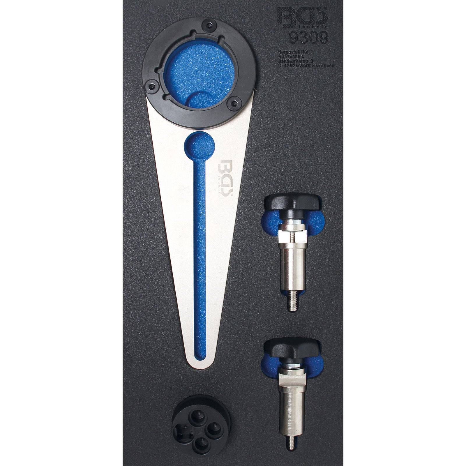 Ein Werkzeugsatz in einem Schaumstoffkoffer umfasst ein großes dreieckiges Werkzeug mit einem blauen Streifen, zwei Metallstifte mit schwarzen Knöpfen und ein kreisförmiges Stück.