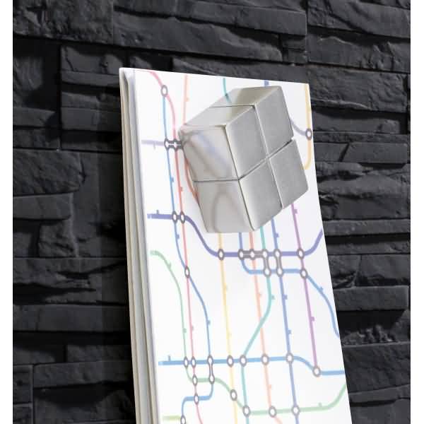 Ein kleiner silberner Würfel, der auf einem weißen Notizbuch mit einem bunten U-Bahn-Karte-Muster vor einer schwarzen Steinwand montiert ist.