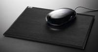 Schwarze Computermaus auf einem geschlossenen schwarzen Laptop oder Gerät, von oben auf einer grauen Oberfläche betrachtet.