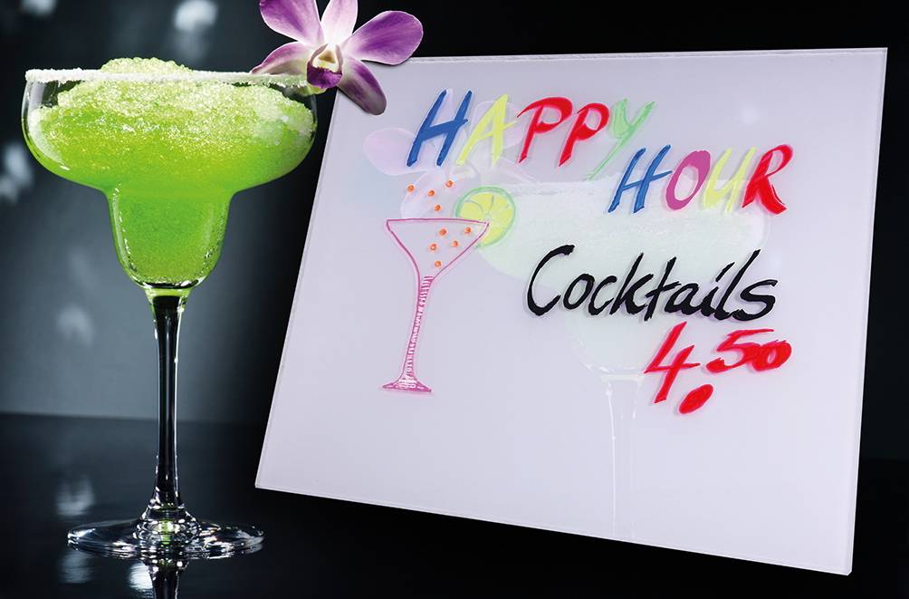 Grüner Margarita-ähnlicher Cocktail in einem Glas mit Salzrand neben einem Schild mit der Aufschrift „HAPPY HOUR Cocktails 4,50