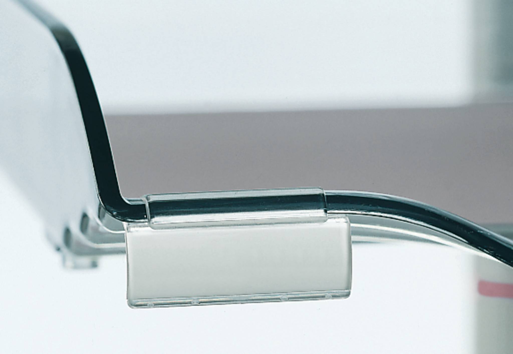 Nahaufnahme einer transparenten Bürostuhlarmlehhne und eines Metallrahmens vor hellem Hintergrund.
