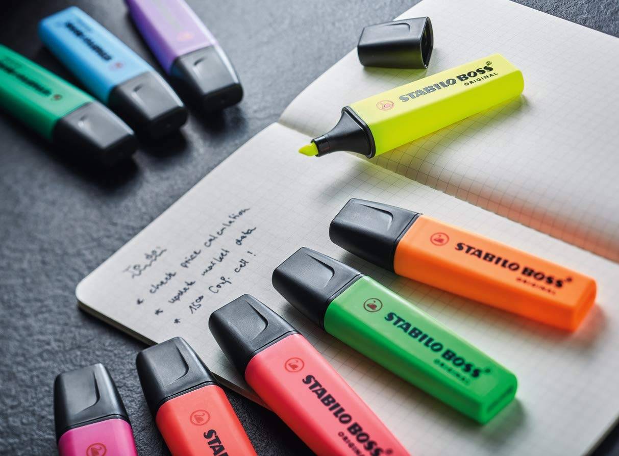 Assortierte STABILO BOSS Textmarker in leuchtenden Farben, die um ein offenes Notizbuch mit handschriftlichen Notizen angeordnet sind.
