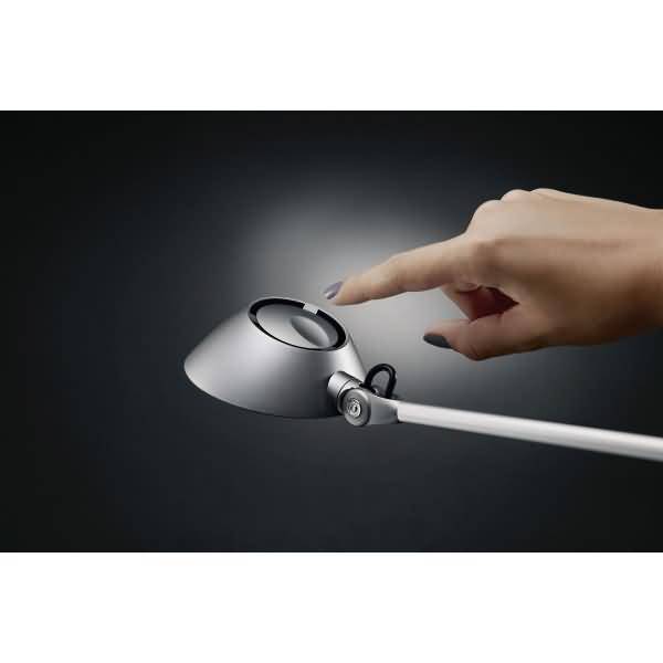 Hand, die sich ausstreckt, um eine moderne weiße Schreibtischlampe zu berühren, was auf berührungsgesteuertes Licht hinweist.