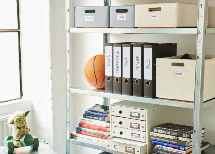 Organisierte Regaleinheit mit beschrifteten Ordnern, Aufbewahrungsboxen, Büchern, einem Basketball und einer Yoda-Figur neben einem Fenster.