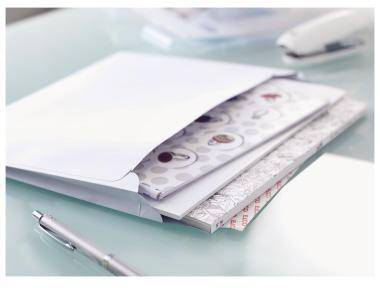 Offener weißer Umschlag mit gemusterten Papierkarten darin, auf einem Schreibtisch liegend mit einem Stift in der Nähe.