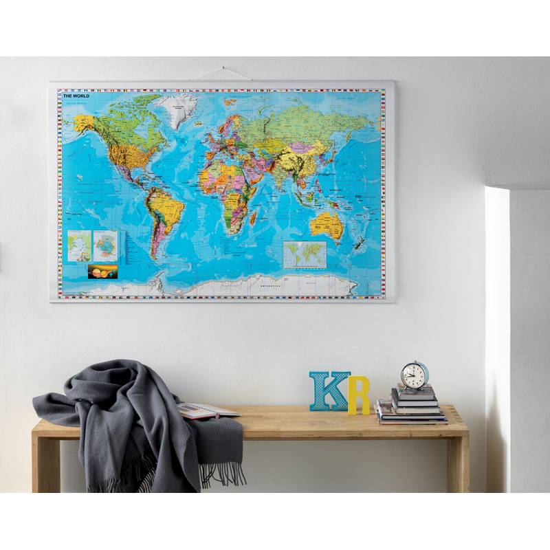 Eine Weltkarte mit farbenfrohen Details hängt an einer weißen Wand über einem Holztisch, auf dem eine graue Decke, die Buchstaben 'K' und 'R' sowie eine Uhr zu sehen sind.