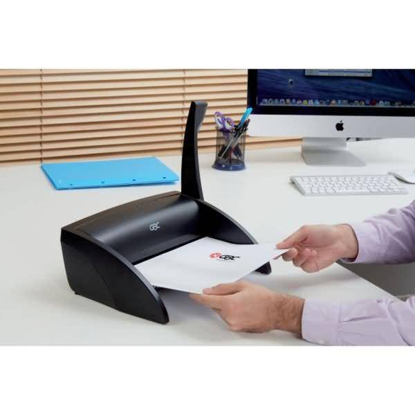 Eine Person füttert ein Dokument in einen Desktop-Scanner auf einem Bürotisch neben einem iMac und einer Tastatur ein.