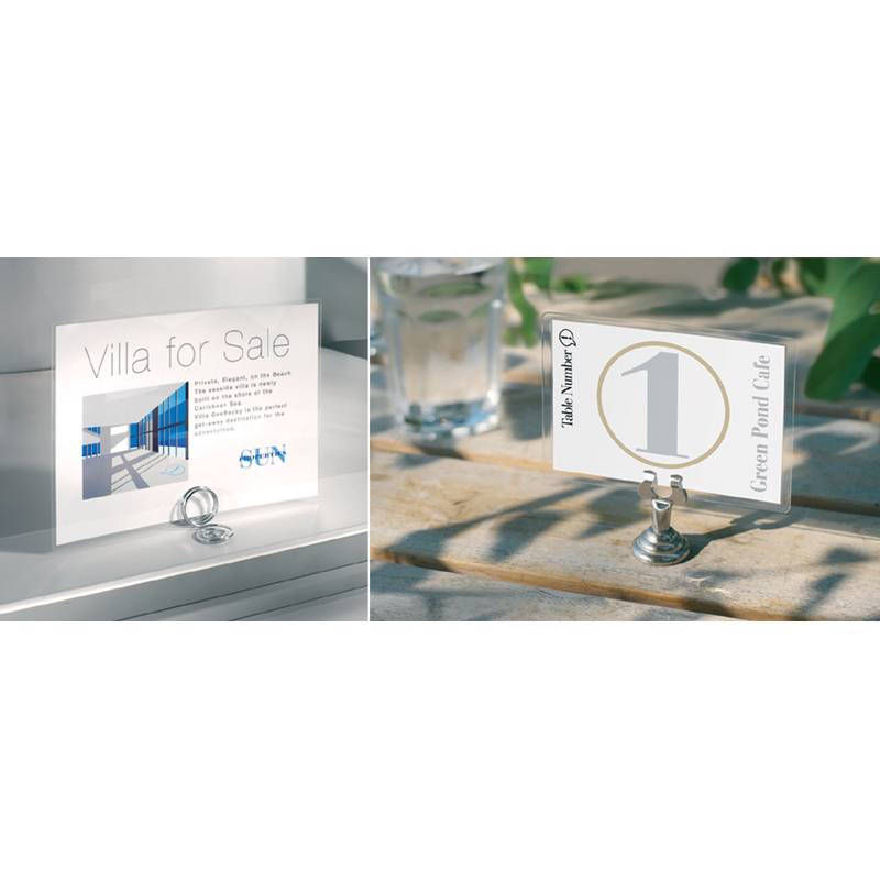 Zwei Karten mit Metallhaltern auf einer Oberfläche. Linke Karte mit der Aufschrift ‚Villa zu verkaufen' mit zusätzlichem Text und einem blauen Logo. Rechte Karte mit der Nummer ‚1' und ‚Green Pond Cafe'.