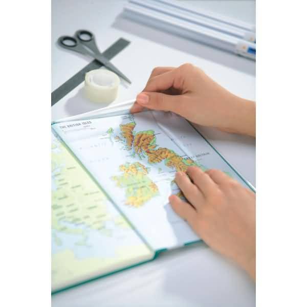 Hände zeigen auf eine Karte in einem offenen Atlas auf einem Schreibtisch, mit Schere, Klebeband und Stiften in der Nähe.