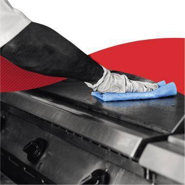 Behandschuhte Hand, die eine schwarze Grill- oder Kochfeld-Oberfläche mit einem blauen Tuch abwischt.