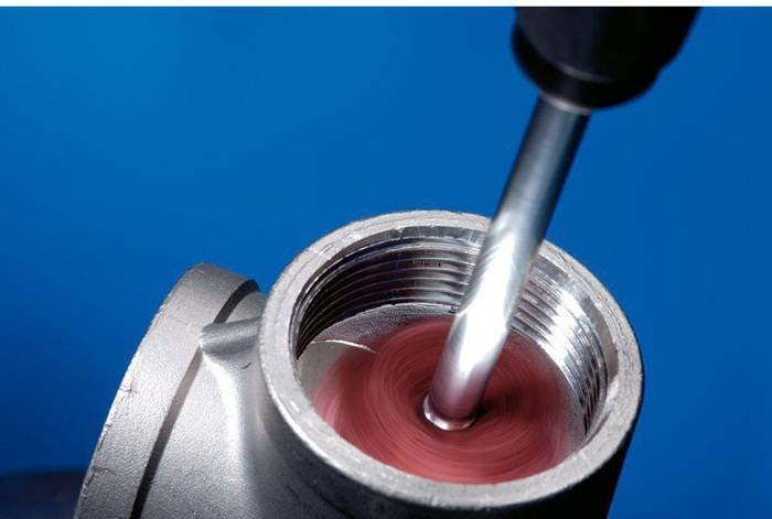 Eine Nahaufnahme eines Werkzeugs, das das Innere eines gerillten Metallrohrs poliert und dabei einen roten Glanz erzeugt, vor einem blauen Hintergrund.