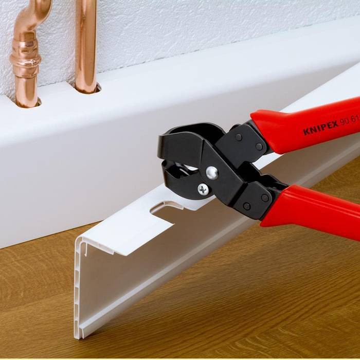 Das Bild zeigt ein Knipex-Werkzeug, das einen Kunststoff-Kabelkanal in der Nähe von Kupferrohren auf einem Holzboden präzise durchtrennt und dabei seine Genauigkeit unterstreicht.