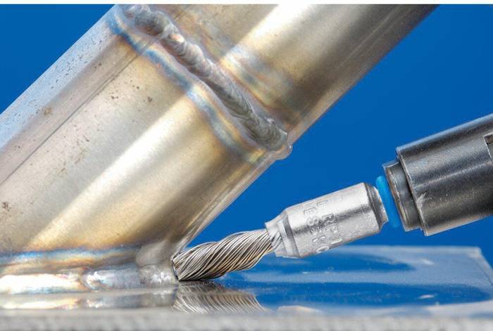 Ein Nahaufnahmebild eines Metallschleifwerkzeugs, das an einer geschweißten Stahlröhre arbeitet, vor einem blauen Hintergrund, wobei die Präzision der Metallbearbeitung zur Geltung kommt.