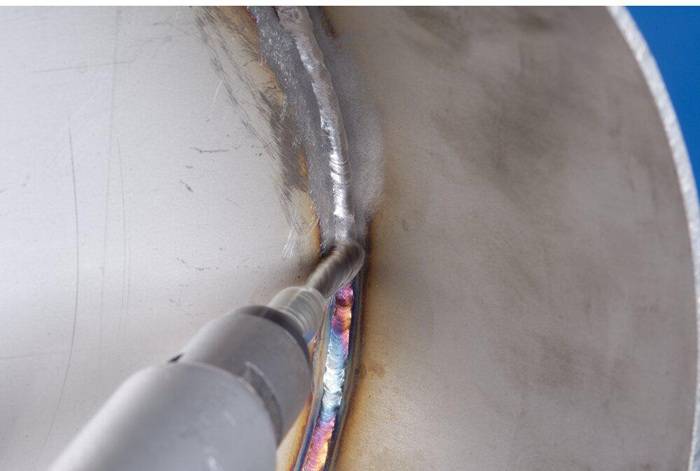 Nahaufnahme eines Schweißvorgangs an einem Metallrohr, die detaillierte Schweißnahtmuster und Oberflächenverfärbungen durch Hitzeeinwirkung zeigt.