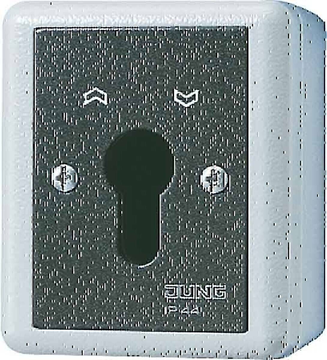 Ein silberner Schlüssellochzylinder mit zwei Schrauben auf einem Schild mit der Aufschrift 'Jung IP 44', versehen mit Pfeilen nach oben und unten, die wahrscheinlich die Schließrichtung anzeigen.