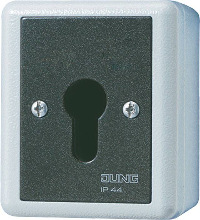 Ein grauer, outdoor Elektro-Wandsteckdosenschutz, beschriftet mit 'Jung IP 44'. Er verfügt über ein Schlüsselloch-Design für sicheren Zugang.
