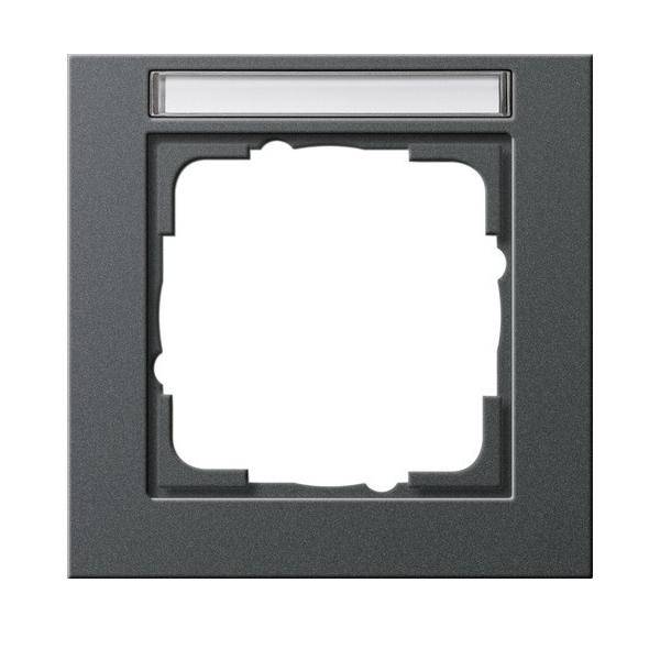 Quadratischer dunkler Rahmen mit zentralem Ausschnitt und horizontalem weißem Streifen oben, wahrscheinlich zur Verwendung als Lichtschalterabdeckung oder ähnliche Armatur.