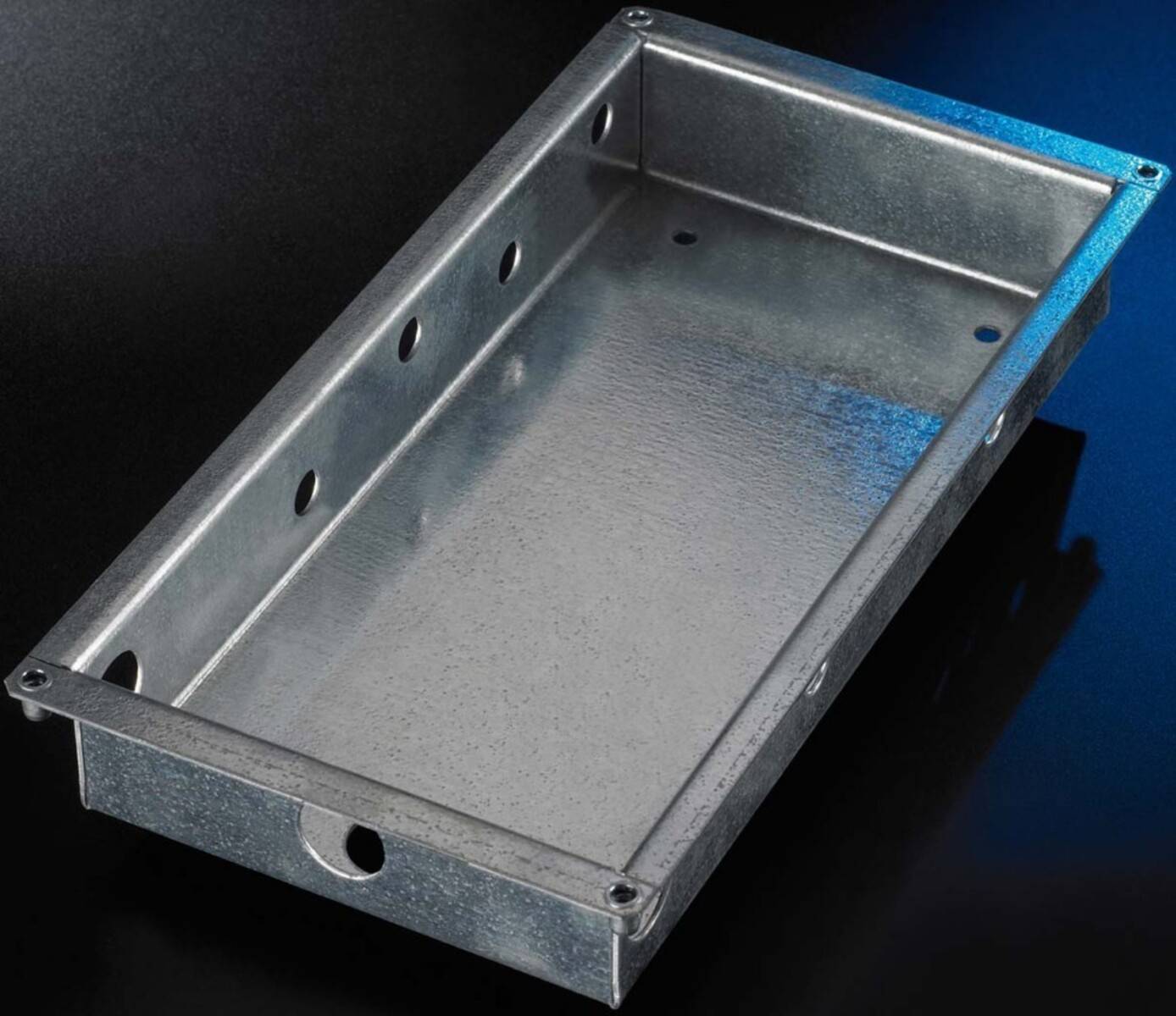 Rechteckige verzinkte Metallfach- oder Gehäusekonstruktion mit erhöhten Seitenwänden und Befestigungslöchern, dargestellt auf dunklem Hintergrund.