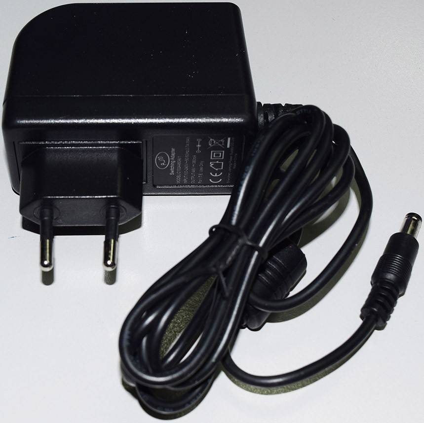 Ein schwarzes Netzteil mit einem zweipinigen Stecker und angeschlossenem Kabel, das in einem Hohlstecker endet, für elektrische Geräte.