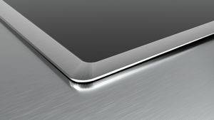 Nahaufnahme einer Laptopecke mit silberner Metallkante und dunklem Bildschirm auf einer gebürsteten Aluminiumberfläche.