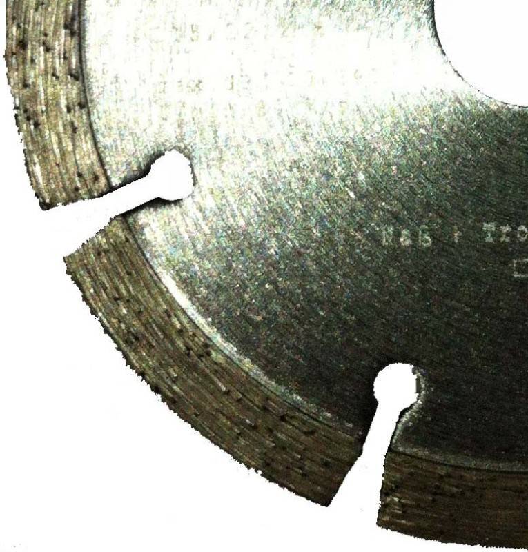 Nahaufnahme eines abgenutzten Kreissägeblattsegments mit zwei großen Montagelöchern und eingravierter Markierungen auf der Metalloberfläche.