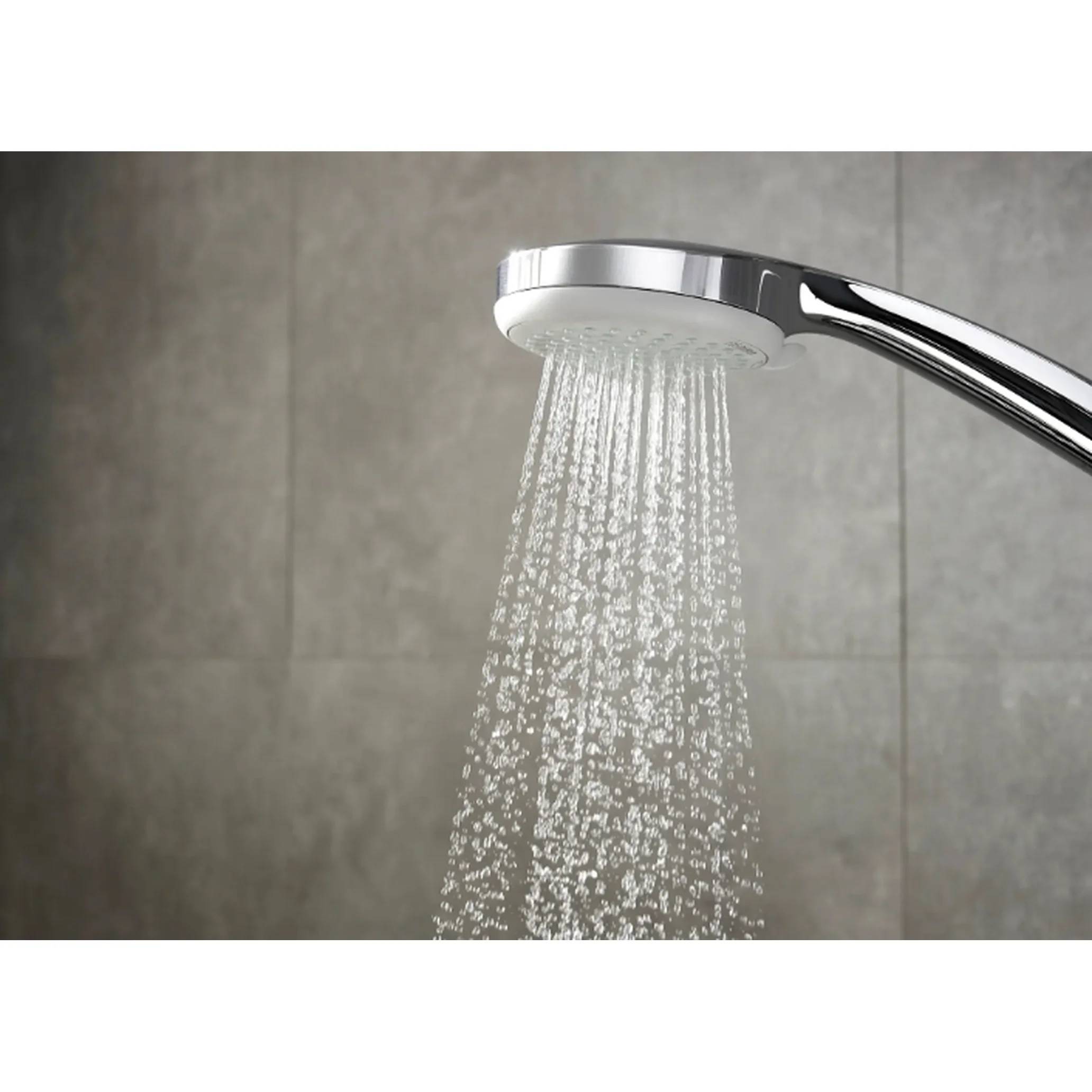 Nahaufnahme eines verchromten Duschkopfes, der Wasser gegen eine grau geflieste Badezimmerwand sprüht.