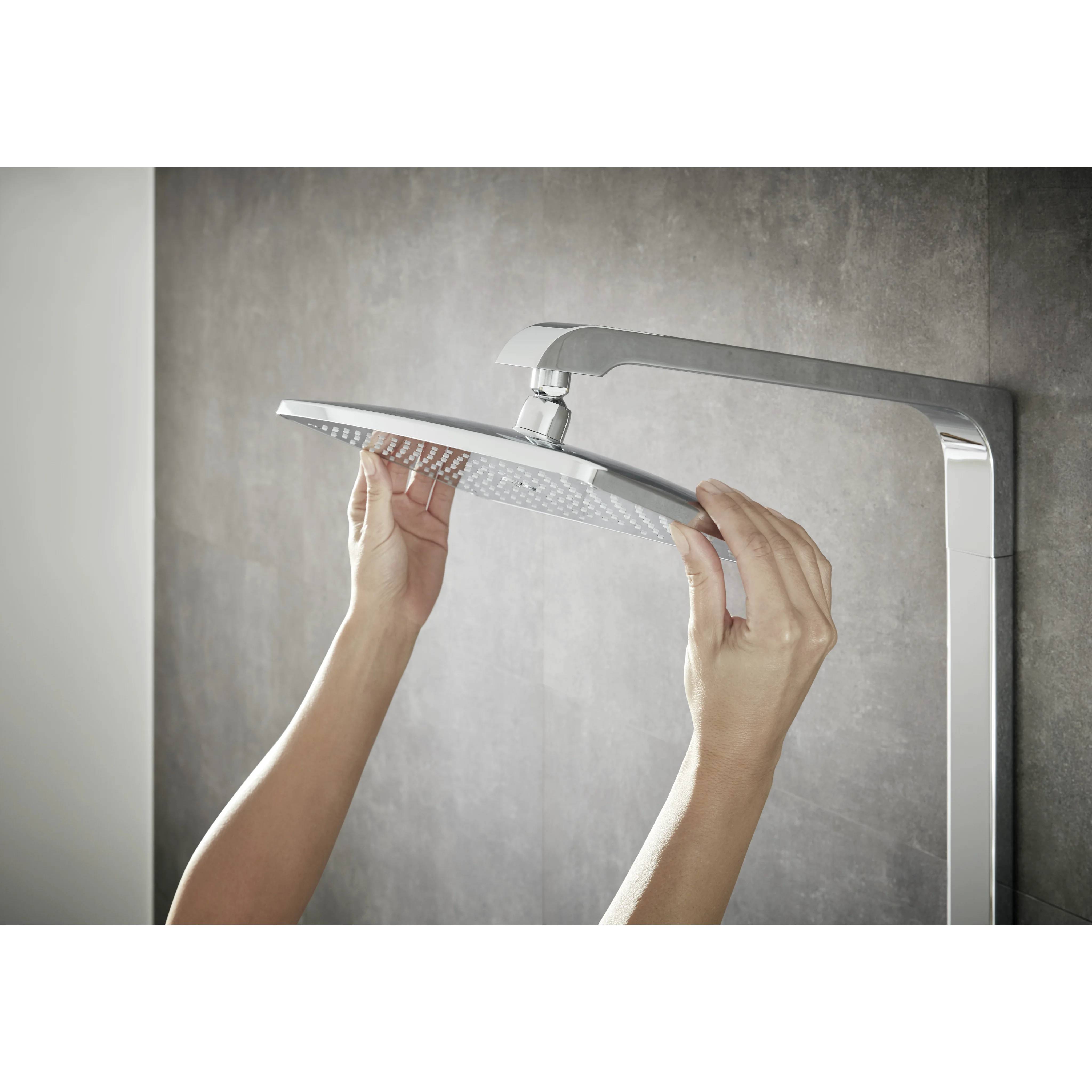 Hände, die einen quadratischen Regenfallduschkopf auf einem modernen verchromten Duscharm vor einer grauen Badezimmerwand einstellen.