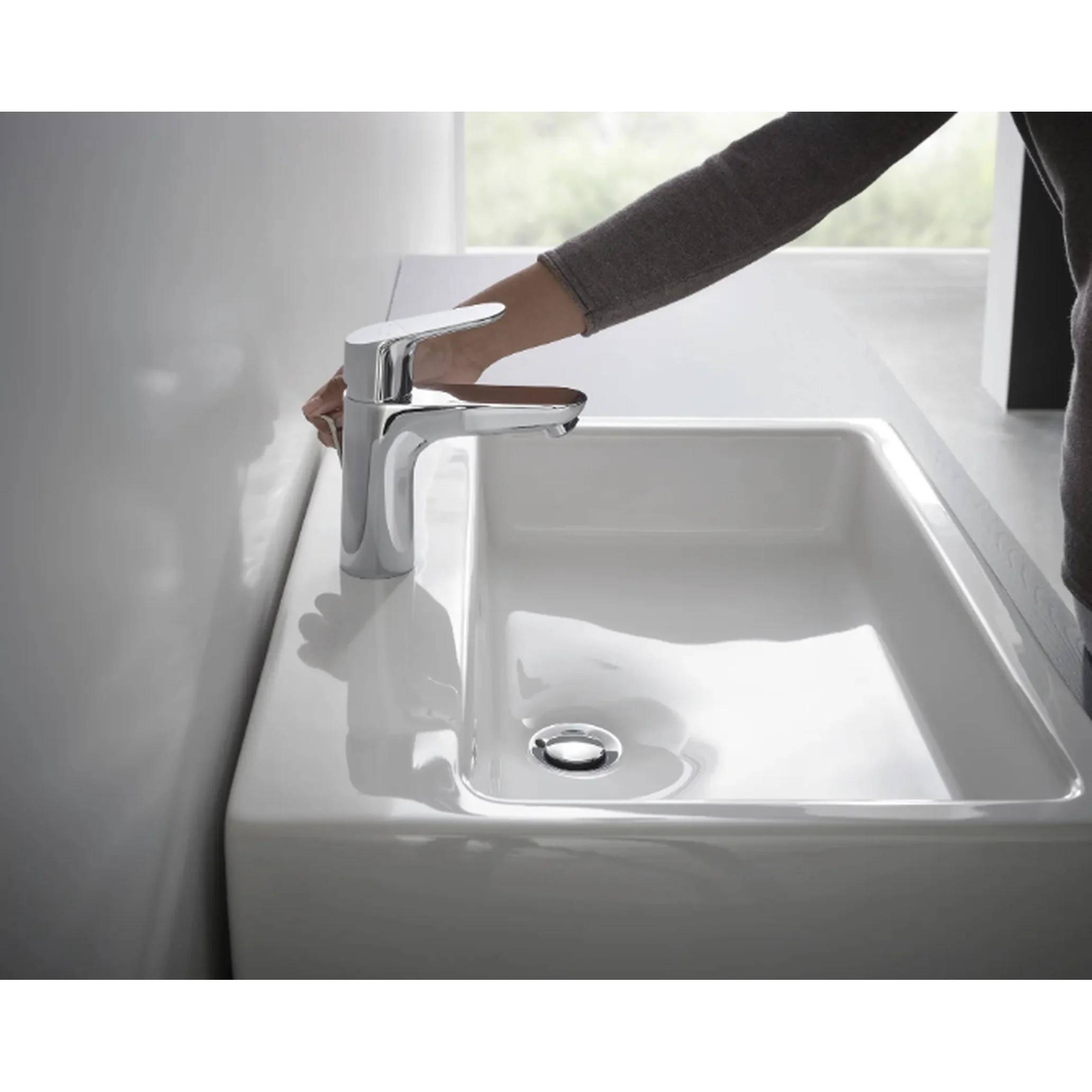 Person, die einen chromglänzenden Badezimmerwasserhahn über einem weißen Waschbecken in einem hellen, modernen Badezimmer einstellt.