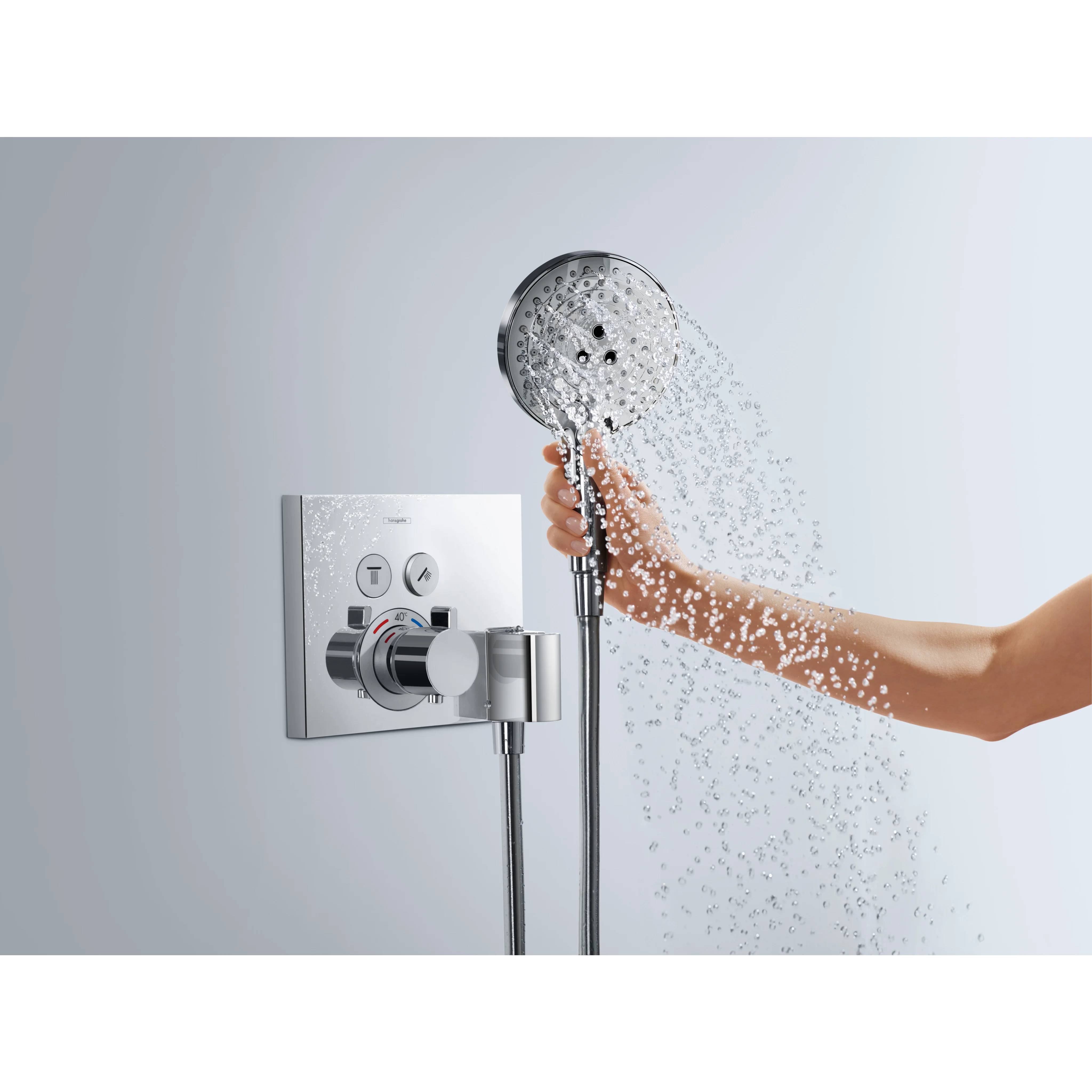 Eine Hand hält einen tragbaren Duschkopf, der Wasser neben einem an der Wand montierten Duschkontrollfeld mit Knöpfen und Schaltern sprüht.
