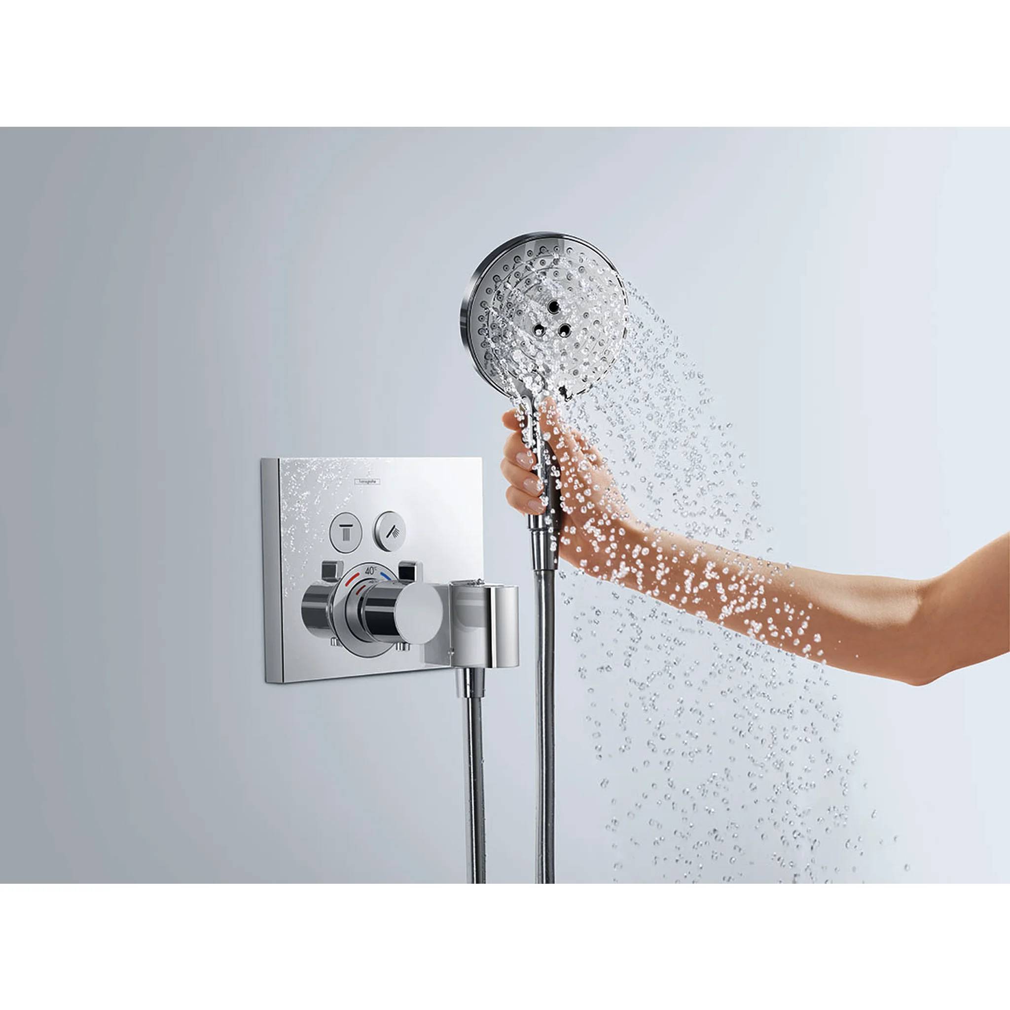 Hand, die einen tragbaren Duschkopf hält und Wasser neben einem an der Wand montierten Duschkontrollfeld sprüht.
