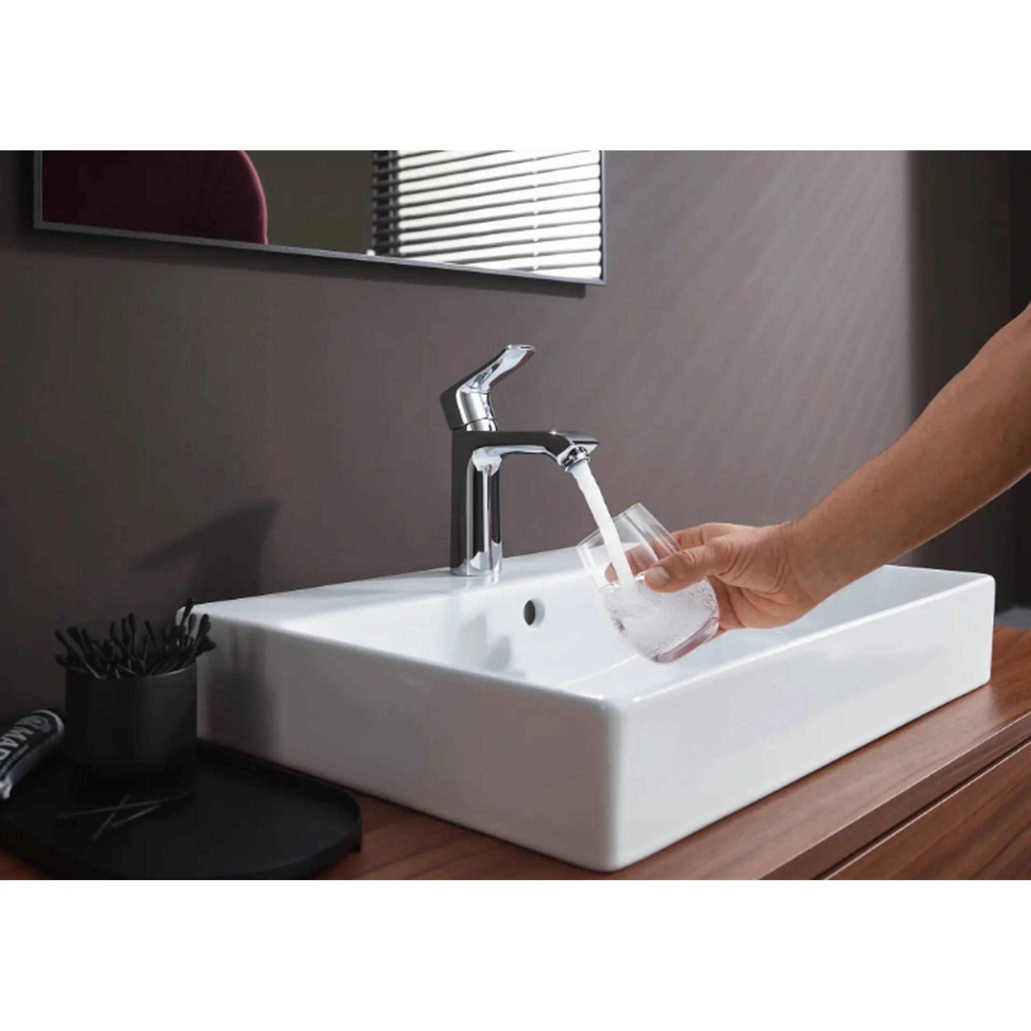 Eine Hand füllt ein klares Glas mit Wasser aus einem Chromhahn über einem modernen Badezimmerbecken.