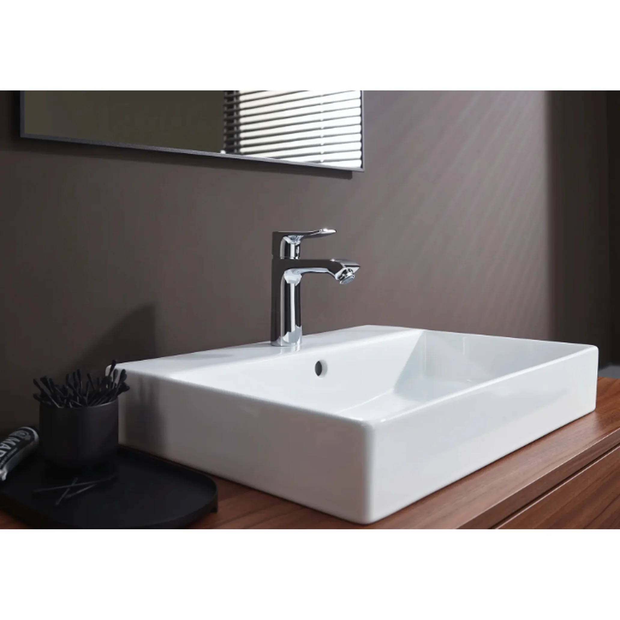 Modernes Waschbecken auf einer Holzarbeitsplatte mit Chromarmatur, Seifenschale und Wandspiegel vor einer taupefarbenen Wand.
