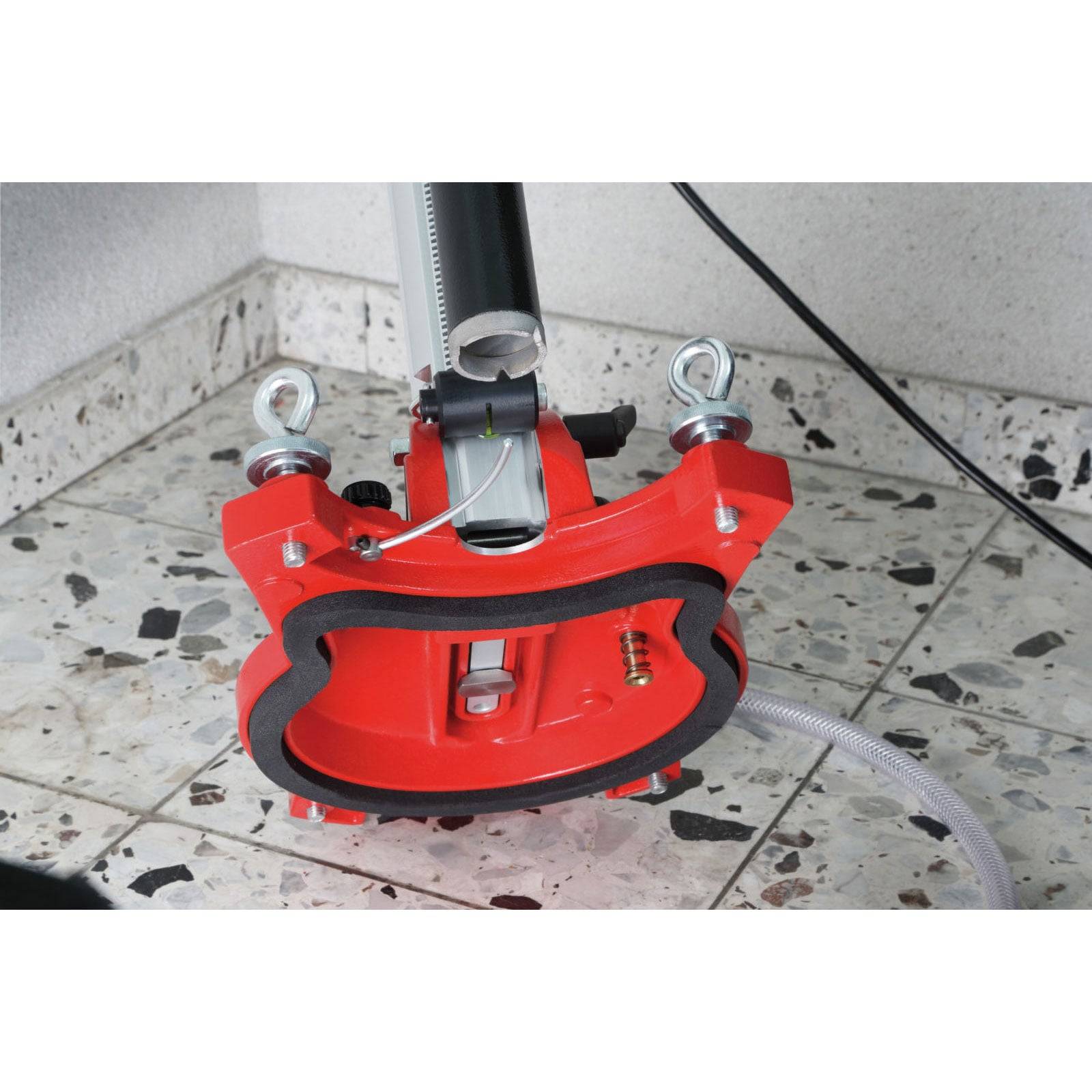 Rotes Gerät mit Metallbeschlägen und einem Schlauch auf einem gefliesten Boden, möglicherweise Ausrüstung für industrielle oder Bauanwendungen.