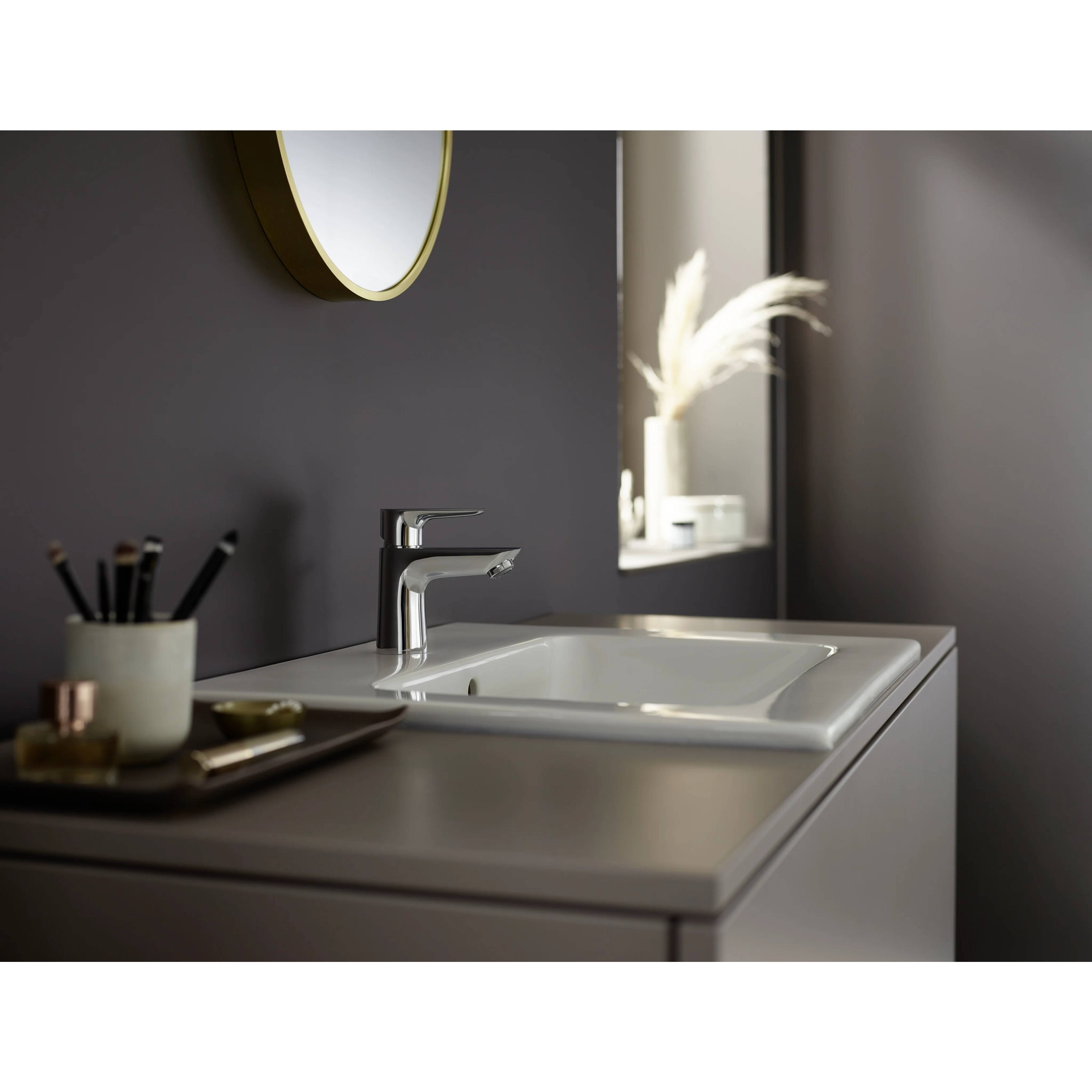 Modernes Badezimmerschrank mit weißem Waschbecken und verchromtem Wasserhahn, daneben ein Spiegel und ein Wandregal mit dekorativer Vase.