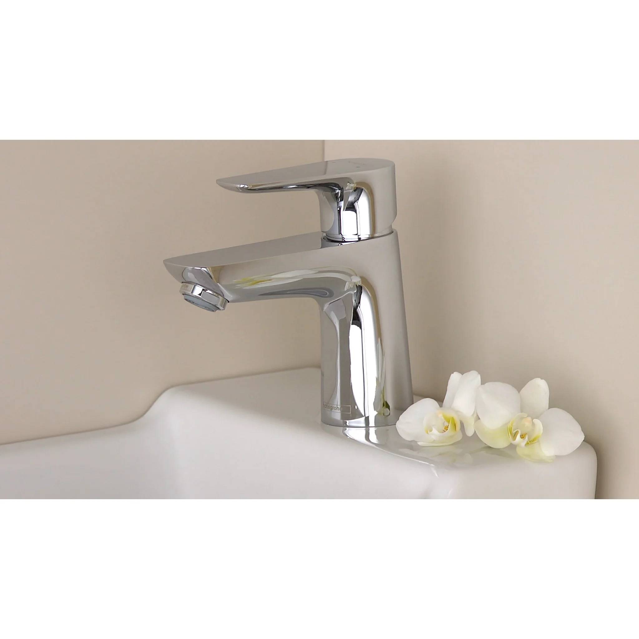 Chromglanz-Badezimmerwasserhahn mit weißen Orchideenblüten, die auf der Waschbeckenkante vor einer beigen Wand platziert sind.