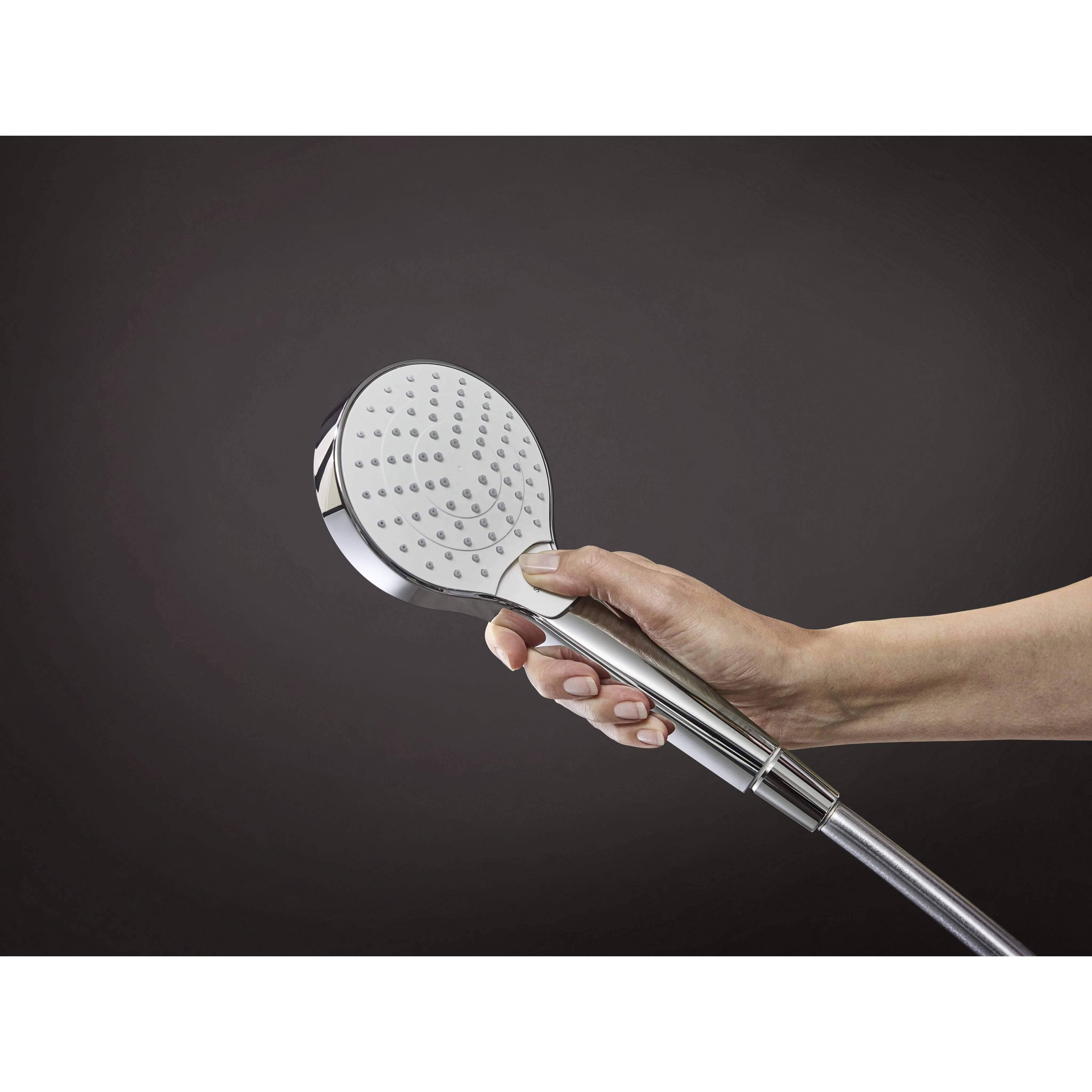 Eine Hand, die einen verchromten Handbrause gegen einen dunklen Hintergrund hält.