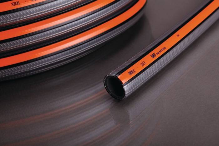 Eine gewickelte schwarze und orangefarbene industrielle Schlauchleitung ruht auf einer glatten, reflektierenden grauen Oberfläche und hebt die Textur und das Design des Materials hervor.