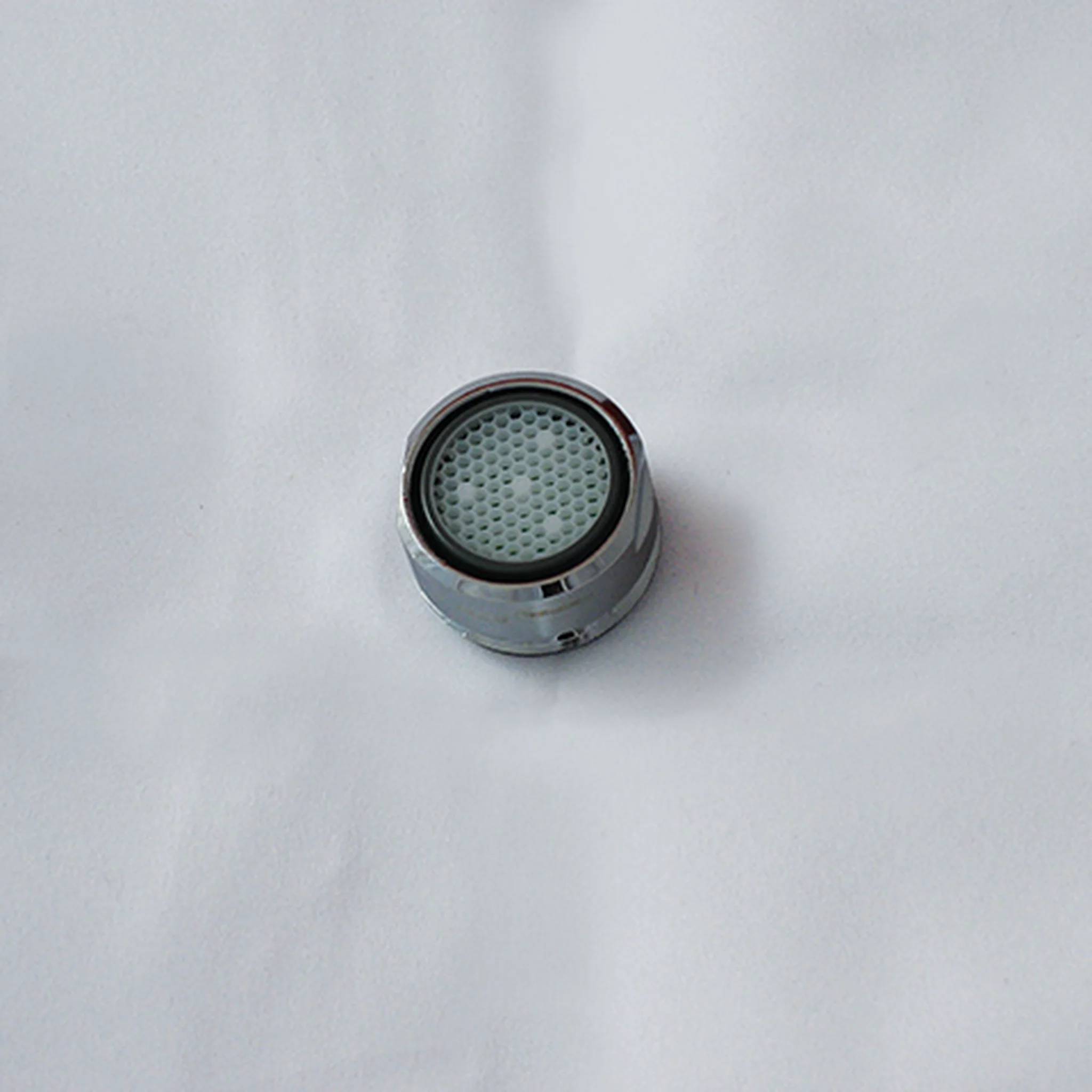 Nahaufnahme eines kleinen Metallnetzfilters oder Belüfters auf einer weißen Oberfläche.